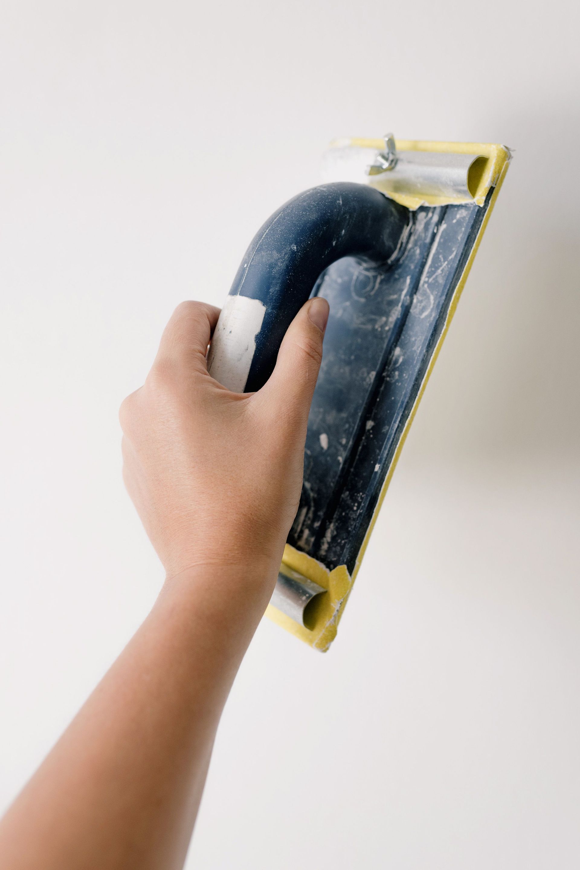 Crop anonymous person holding scraper and working with wall at home during renovation